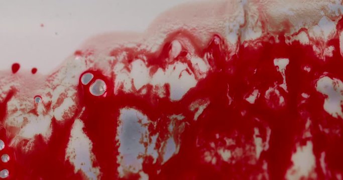 Sticky red gooey liquid resembling blood sliding down a viscous white surface with a few bubbles. 4K