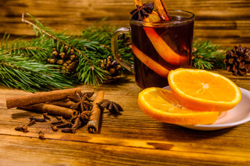 Cup of mulled wine with cinnamon, sliced orange and fir tree branches on wooden table