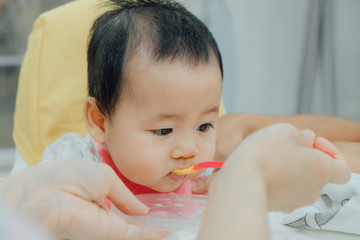 feeding 6 months asian baby girl on high chair. mom feeds blend food to her daughter.Traditional Weaning