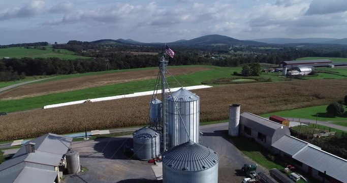 Aerial view pushing in towards American flag at top of grain silo with cornfields and mountains in the distance.s