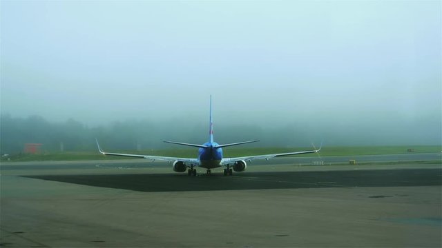 A blue and white airplane slowly starts to move towards the runway on a foggy day at Stockholm Arlanda. No camera movement. Filmed in UHD 4K.