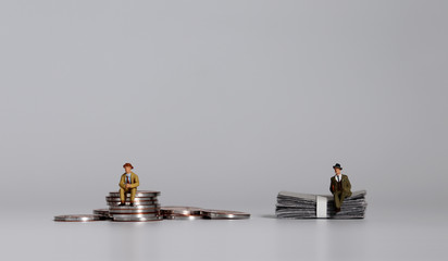A miniature man sitting on a pile of coins and a miniature man sitting on a pile of bills.
