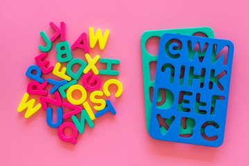 Alphabet for kids concept. English letters in disorder near stencil on pink background top view