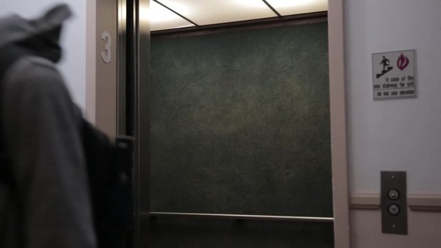 College student boy gets off elevator to go to his apartment. Wearing backpack and just got done with school and class.