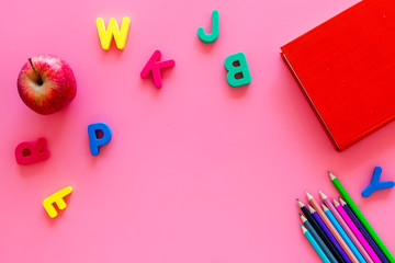 Primary school concept. Letters of english alphabet, book, apple and color pencils on pink background top view copy space