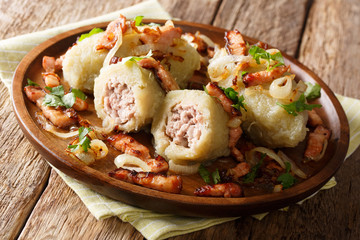 Freshly cooked Cepelinai potato dumplings with minced meat served with bacon, parsley and fried onions close-up on a plate. horizontal