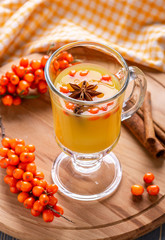 Hot beverage of sea-buckthorn berries in glass cup on wooden background. Rustic style.