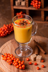 Hot beverage of sea-buckthorn berries in glass cup on wooden background. Rustic style.