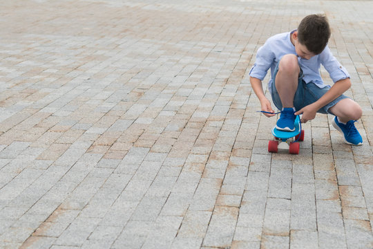 boy on blue skateboard tying shoelaces on sneaker