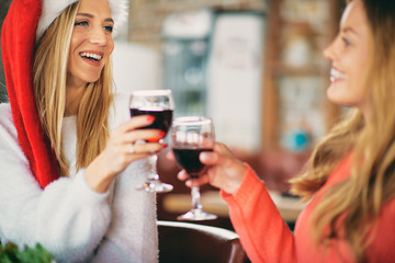 Girlfriends making a toast on Christmas eve while sitting at table. Christmas and winter holidays concept.