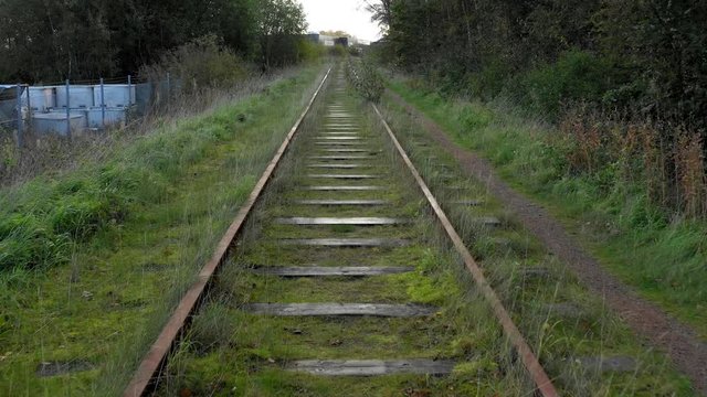 Following old rusty abandoned rail tracks. Grass and trees on the side. MOVING FORWARD.