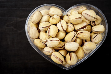 glass bowl in the shape of a heart full of delicious pistachios on an old wooden black table in a pub