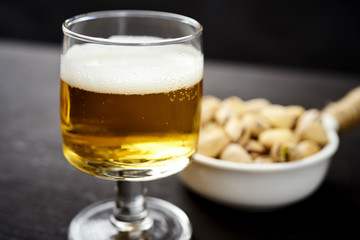 delicious beer in a glass and pistachios in a white bowl on an old black table