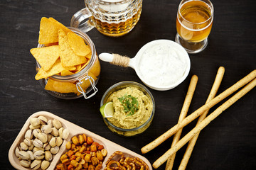 beer and a bowl of guacamole with nachos and salty snacks on an old black wooden table in a pub