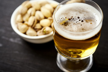 delicious beer in a glass and pistachios in a white bowl on an old black table in a pub