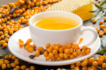 Sea buckthorn, honeycomb with honey and cup of  tea on black stone table.