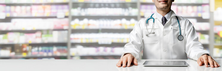 Male pharmacist sitting at table with tablet computer in pharmacy office. Medical healthcare staff and drugstore business.