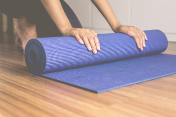 Woman hand rolling or folding blue yoga mat after a workout,Exercise equipment.Healthy fitness and...