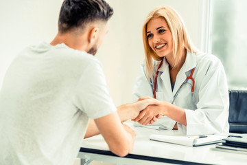 Woman doctor doing handshake with male patient in hospital office room. Healthcare and medical...