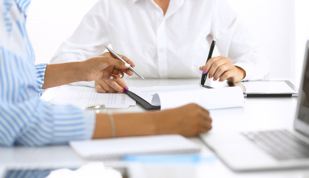 Two female accountants checking financial statement or counting by calculator income for tax form, hands at meeting close-up. Internal Revenue Service inspector checking financial document. Planning