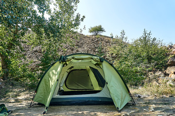 the assembly of a green tourist tent during the halt of tourists on the edge of the forest with stones on a sunny summer day
