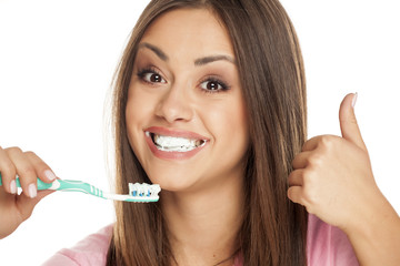 young woman holding  tooth brush on white background and showing thumbs up