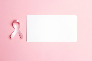 Pink ribbon with blank paper card on pink background. Breast cancer awareness symbol.