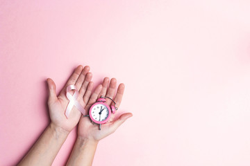 Girl hands holding pink breast cancer awareness ribbon and alarm clock. Copy space for text or...