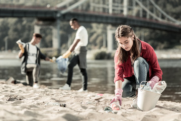 Empty bottles. Beautiful first year student wearing bright pink gloves gathering empty bottles on...