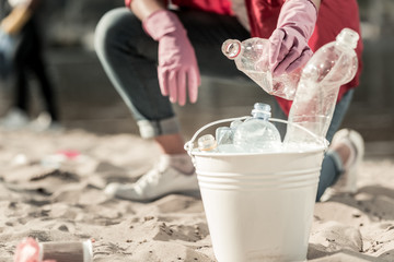 Gloves and bottles. Close up of woman wearing white sneakers and pink gloves gathering empty...