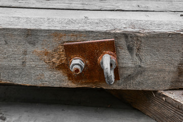The nut fastens a metal rusty plate with a loop to a wooden bar