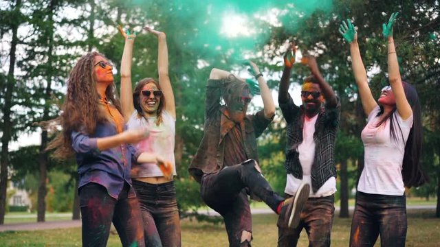Slow motion of multiethnic group of friends students jumping and throwing paint powder then dancing and laughing in bright clouds. Nature, party and fun concept.