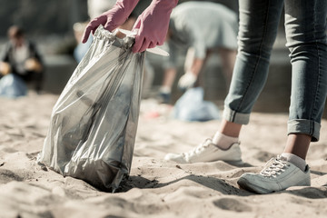 Trash on beach. Close up of young student wearing dark blue jeans and white sneakers cleaning up trash on the beach