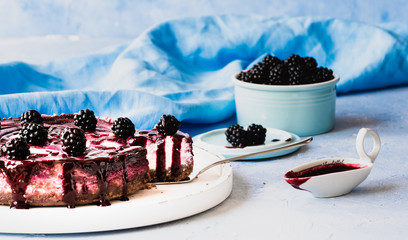 brombeer-cheesecake käsekuchen angeschnitten und fertig zum servieren auf blauem hellen Untergrund...