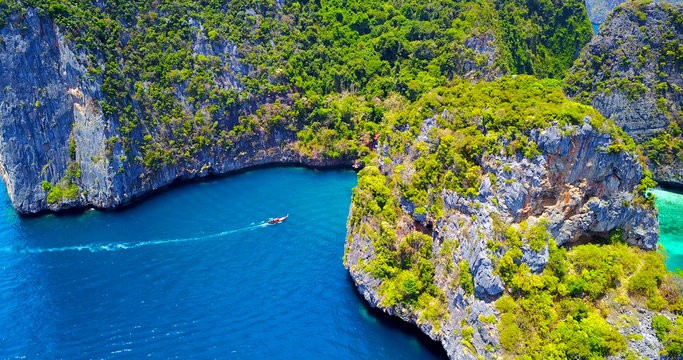 Single Boat Entering Tropical Cove Surrounded by Steep Rocky Islands - Aerial Overhead View - Loh Samah Bay, Thailand