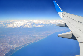 Beautiful view of earth and sea under the wing of plane. Costal city view from above. Travel concept. Freedom concept.