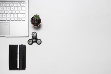 Minimal modern workspace. Composition with laptop, cactus, notebook with pen and fidget spinner isolated on white desk. Top view, flat lay for designers, bloggers, articles - obrazy, fototapety, plakaty