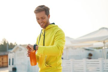 Sportsman with bottle of water is resting and checking his smart