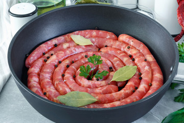 Meat sausages in frying pan, with bay leaves and fresh herbs in the kitchen