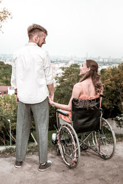 Beautiful view. Calm pretty wheelchair user sitting in the park and looking at her handsome boyfriend