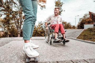 Funny ride. Positive active young man sitting in his wheelchair and smiling while looking at the...
