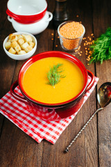 Lentil soup, red ceramic saucepan, wooden background, legumes, home cooking