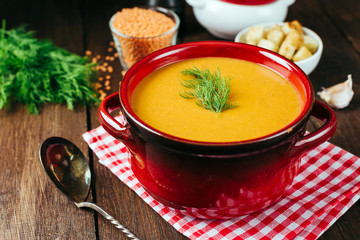 Lentil soup, red ceramic saucepan, wooden background, legumes, home cooking