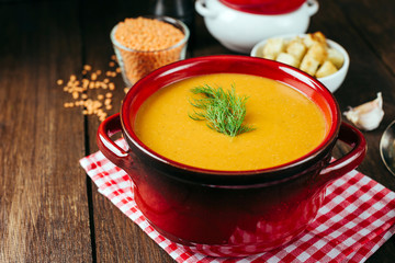 Lentil soup, red ceramic saucepan, wooden background, legumes, home cooking