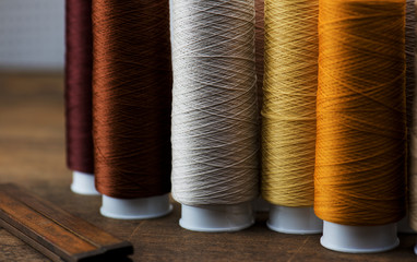 brown, beige, tan colored sewing thread spools on a old work table. Shallow depth of field. Intentionally shot in low key.