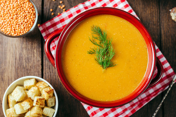 Lentil soup, red ceramic saucepan, wooden background, legumes, home cooking