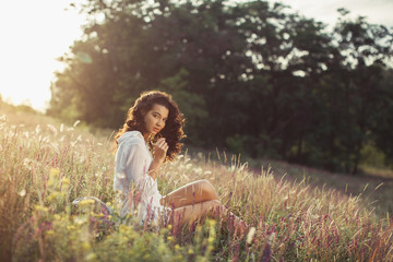 Naklejka na ściany i meble Beautiful Young Woman sitting on the field around wild flowers outdoors. Enjoy Nature. Healthy perfect smiling girl on summer lawn. Allergy free concept. Gorgeous slim mixed race Caucasian Asian model
