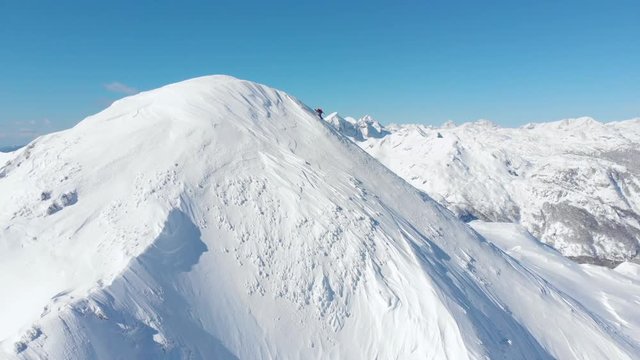 Aerial unrecognizable skier hiking up the snowy mountain in sunny winter