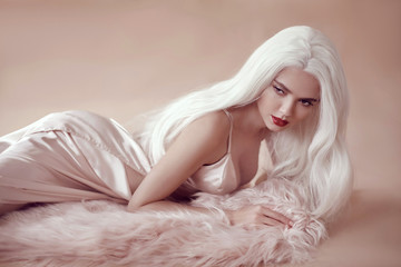 Fashion studio portrait of beautiful blonde sexy girl with long blond hair in beige dress lying on...