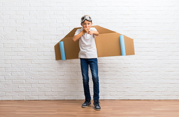 Boy playing with cardboard airplane wings on his back pointing with finger at someone and laughing a lot